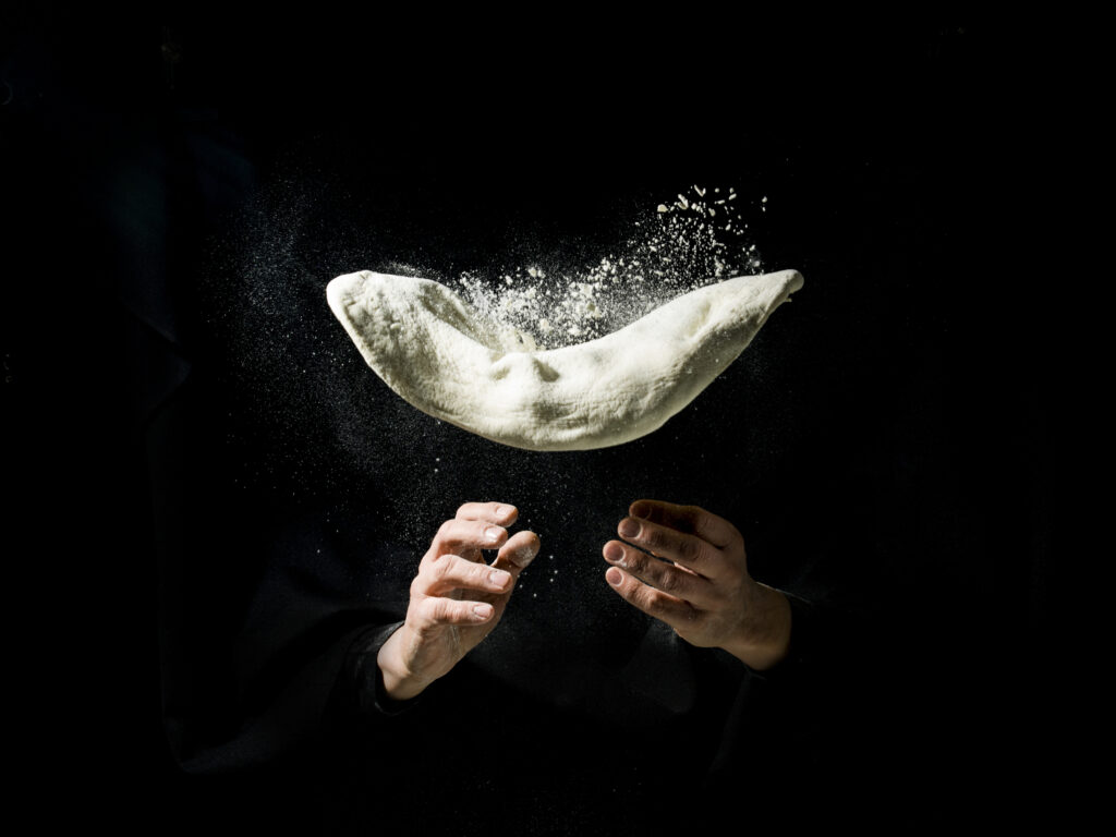 Fliying pizza dough with flour, on drak background