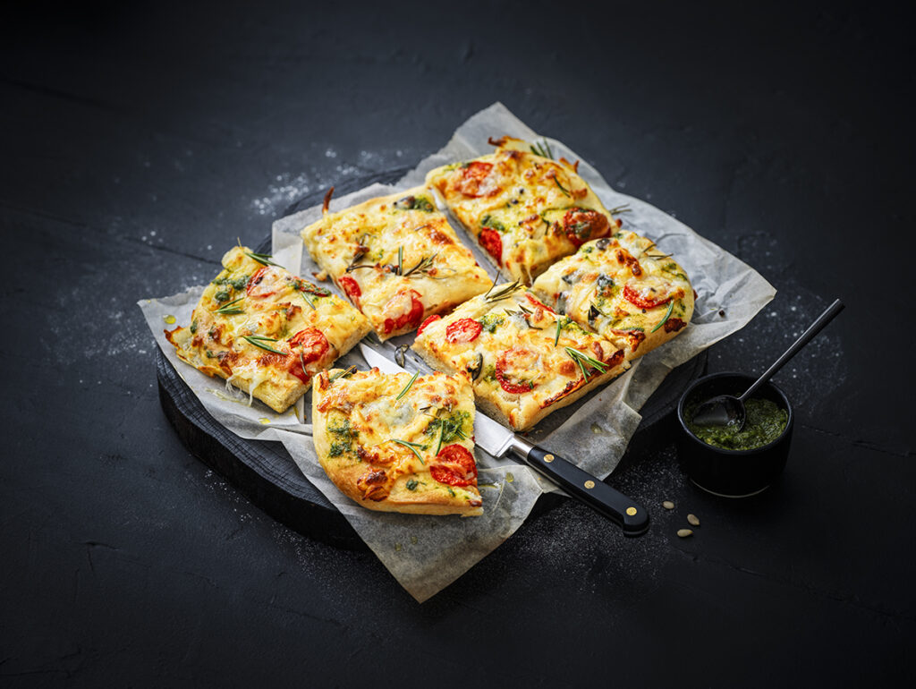 Gourmet square-cut focaccia topped with melted Maestrella mozzarella, cherry tomatoes, and fresh herbs, baked to a perfect golden brown for professional catering.