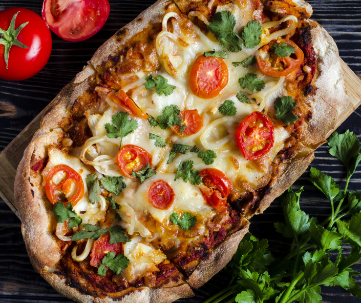 Rustic Roman-style flatbread pizza topped with melted mozzarella, cherry tomatoes, caramelised onions and fresh coriander on a wooden board, illustrating versatile cheese melt performance for creative professional foodservice menus.