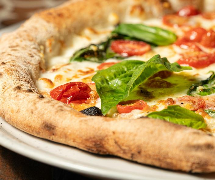 Close-up of a gourmet Neapolitan-style pizza with a thick charred crust, melted mozzarella, fresh cherry tomatoes and basil leaves, showcasing premium cheese quality and melt consistency for professional pizzeria operations.