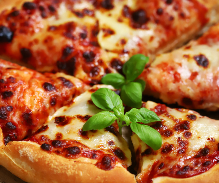 Close-up of golden baked pizza slices with melted mozzarella, rich tomato sauce and fresh basil, showcasing superior cheese melt performance for professional foodservice pizza menus